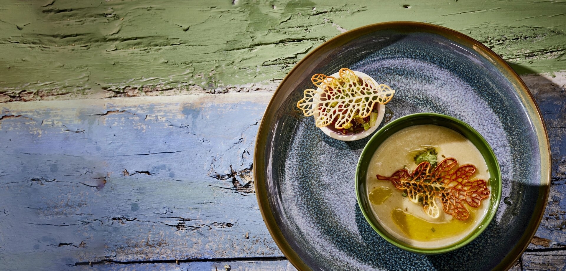 Sellerie Suppe mit herbstblättern serviert auf grün blauem tisch