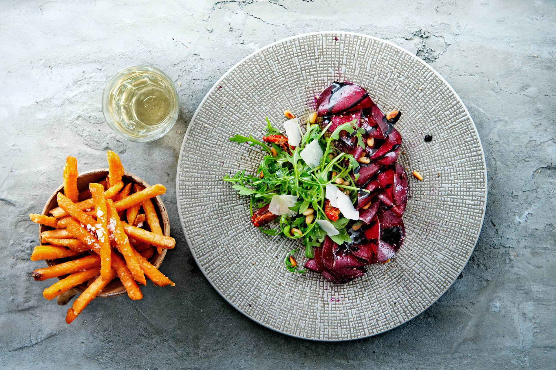 Rote Bete Tagliata serviert mit Süsskartoffelpommes auf grauem Hintergrund und Teller