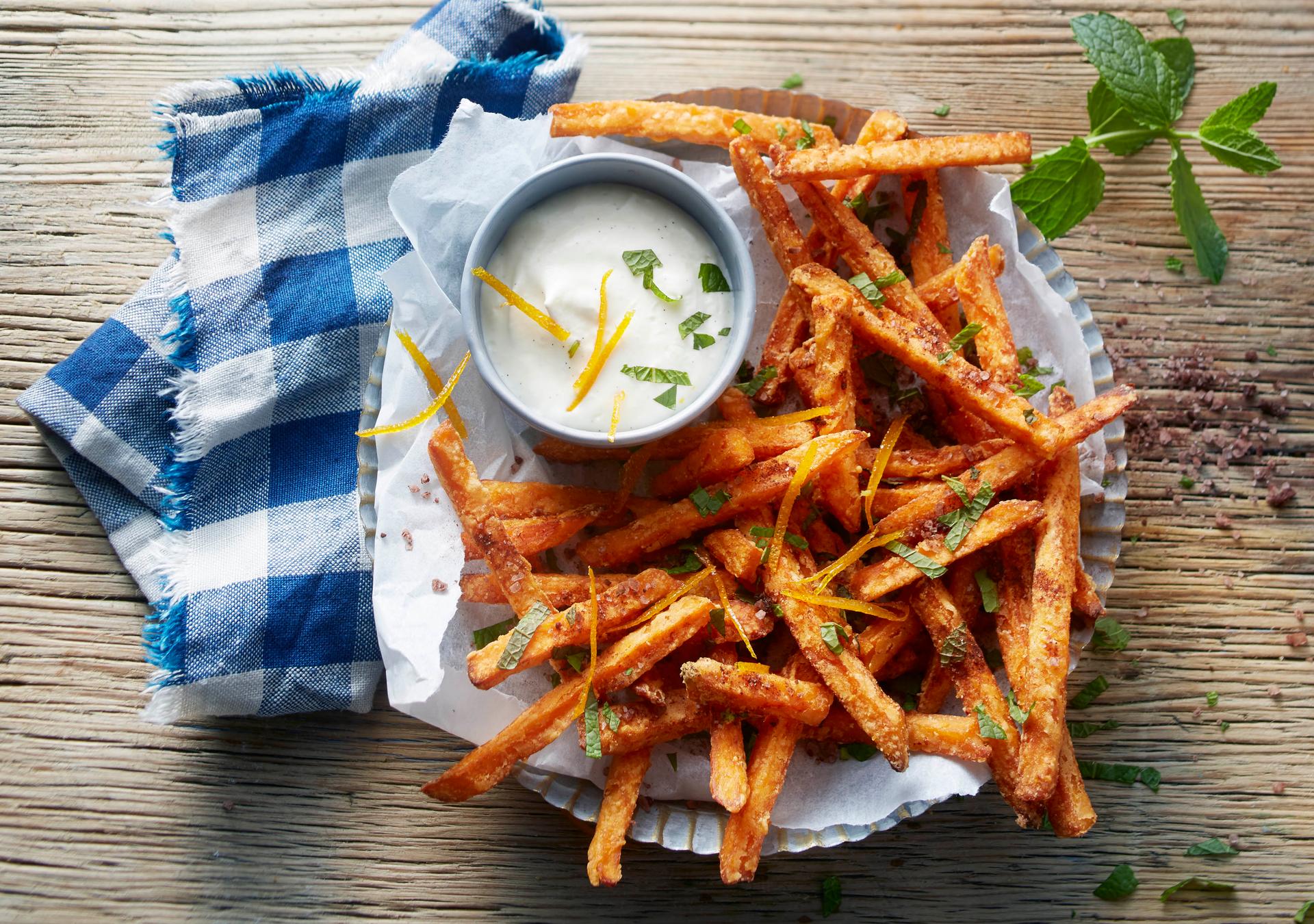 Süsskartoffel-Pommes-Dessert serviert auf Holztisch mit Blau-weissem Küchenhandtuch und Dip