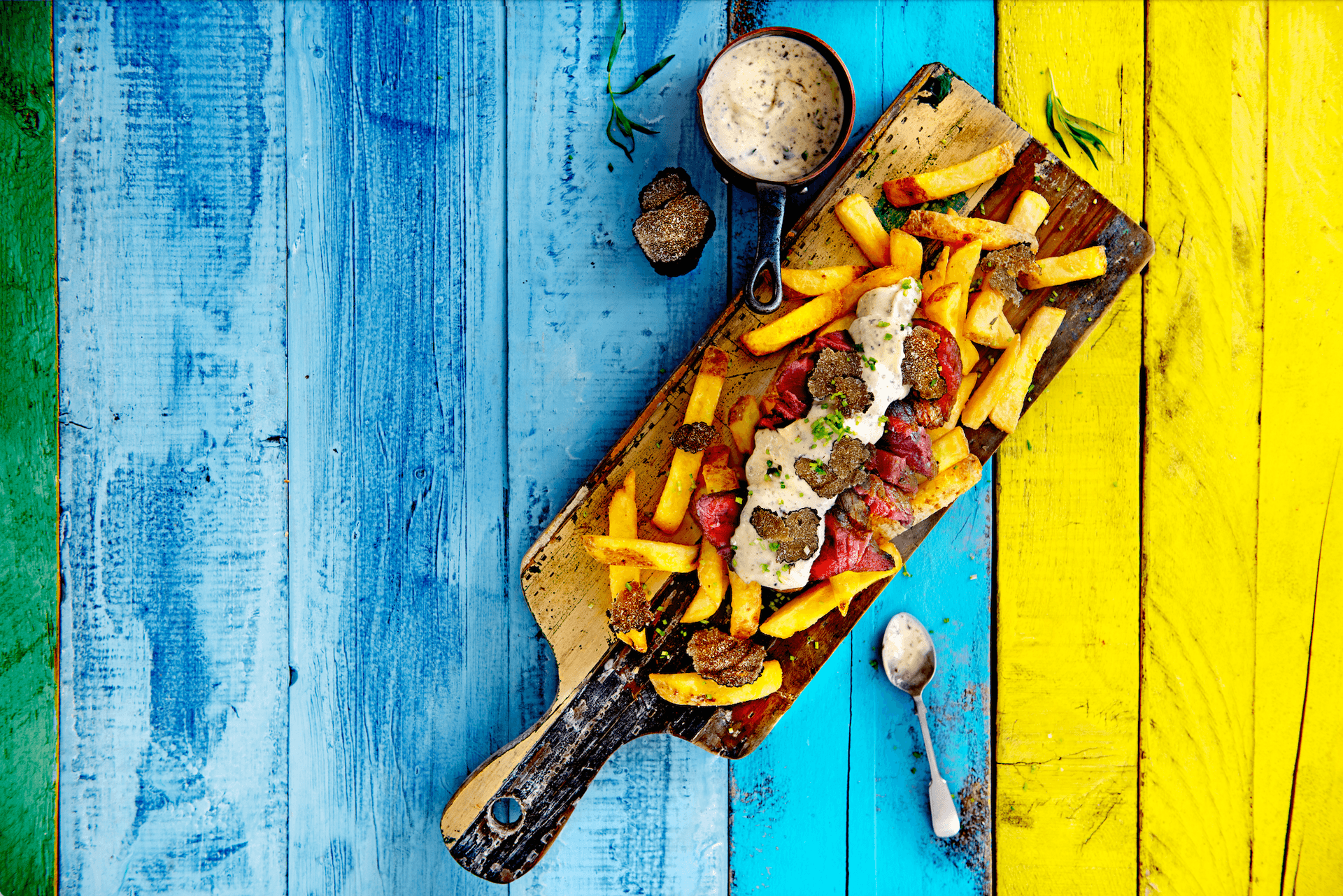 steak & trüffel loaded fries auf blau gelbem holzisch und holzbrett serviert